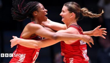 Fran Williams and Olivia Tchine, wearing England's red netball jersey, celebrate after beating South Africa to reach the semi-final by jumping in the air and hugging each other