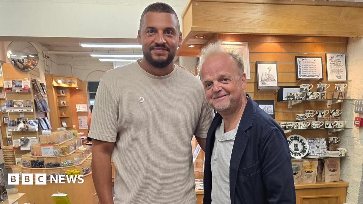 Ben Miller, a man with short dark hair, a beard and a beige shirt, stands next to actor Toby Jones, who is wearing a white shirt and dark blue jacket. They are both standing in a pottery gift shop.