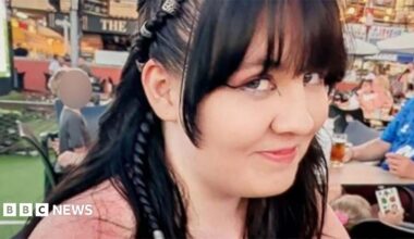 Lilly Jones, who has black hair and is wearing a pink top. She has a fringe and pair of her long hair is tied into a braid.