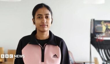A young woman in a pink and black top stands next to a table tennis table.