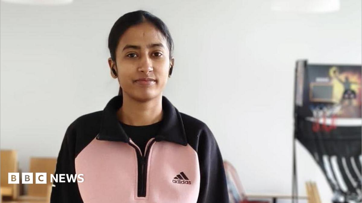 A young woman in a pink and black top stands next to a table tennis table.