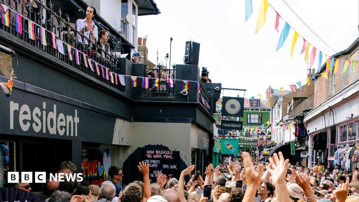 Singer Nick Cave plays a show with his band on the roof of a record shop in Brighton. The street below is swamped with fans.