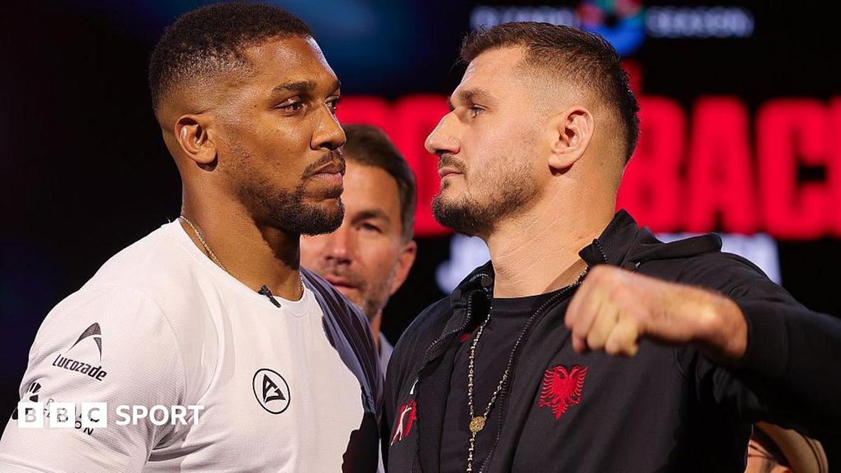 Anthony Joshua and Kristian Prenga face off as they look each other in the eye, Joshua wearing a white top and Prenga in a black hoodie