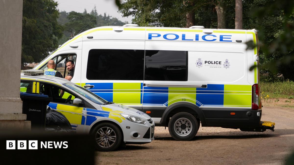 A large police van and a police car parked next to each other. Two officers - including one in the passenger seat and one standing outside - talking