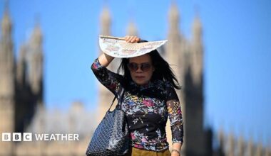 A woman in bright sunlight shades her face with a patterned paper fan