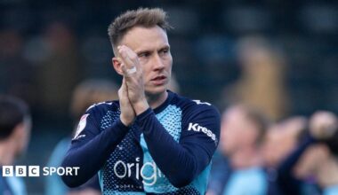 Cauley Woodrow, wearing the light and dark blue quarters of Wycombe Wanderers, claps the fans