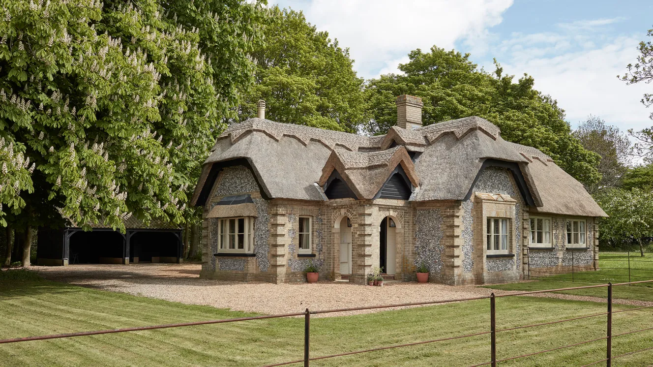 Suffield Lodge, Gunton Estate, with a thatched roof and stone walls, nestled among trees.