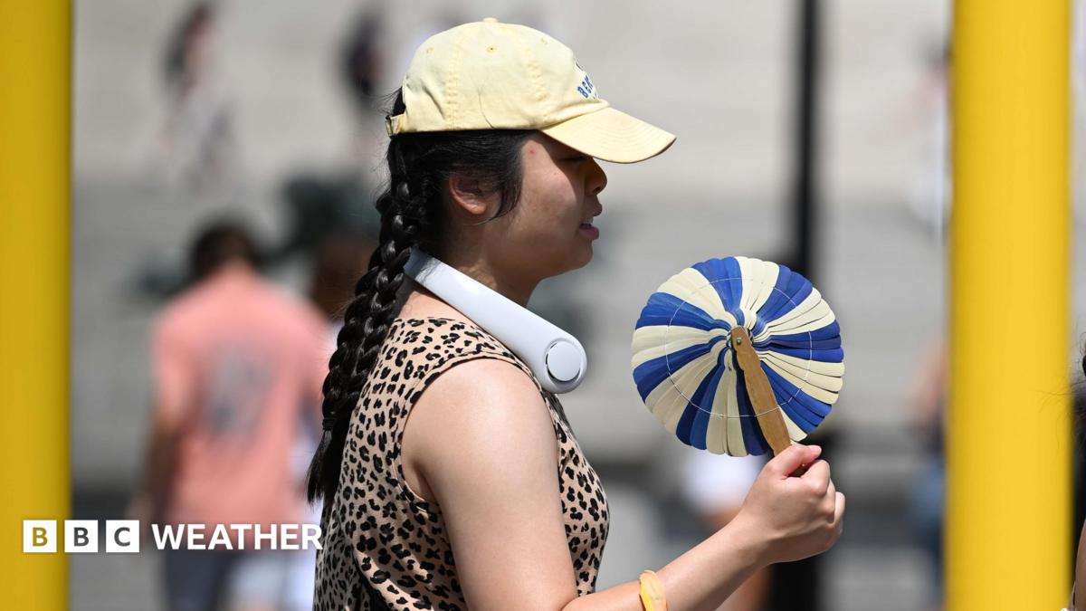 A woman cools herself with a handheld fan whilst walking in the street.
