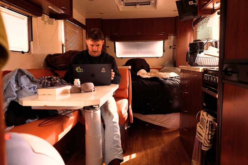 Luke Bateman works on a laptop inside a caravan.