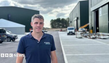 Harvey Mash, wearing a blue polo shirt with his company logo on his left breast stands outside film sound stages at Bovingdon Airfield Studios.