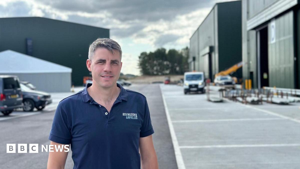 Harvey Mash, wearing a blue polo shirt with his company logo on his left breast stands outside film sound stages at Bovingdon Airfield Studios.