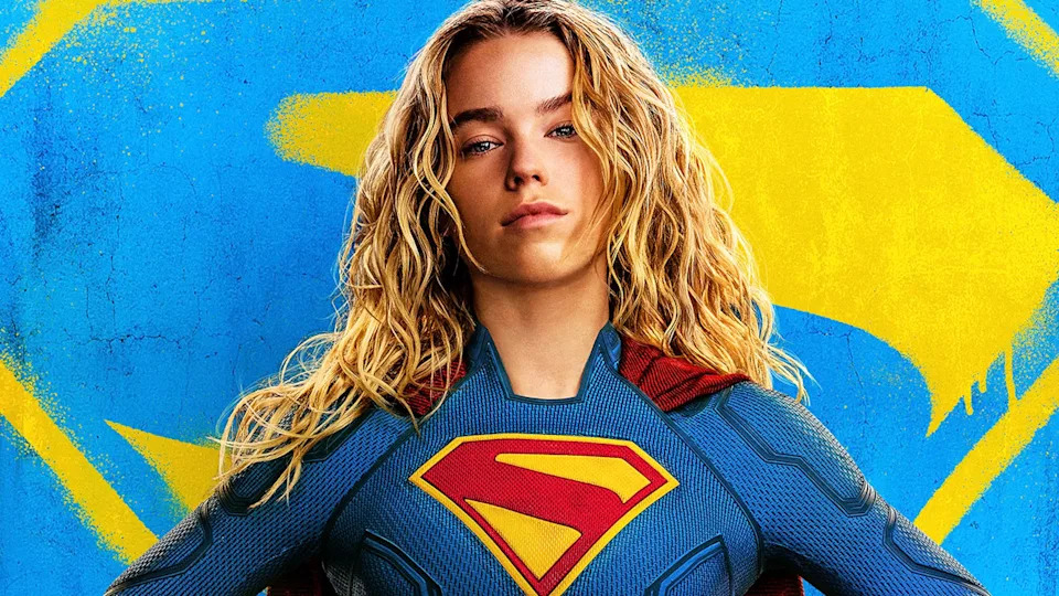 Supergirl in costume in front of blue and yellow logo in Supergirl poster