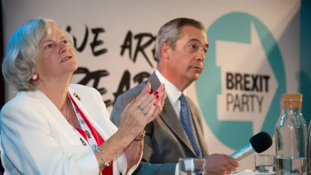 Ann Widdecombe sitting next to Nigel Farage in front of a "Brexit Party" logo on stage
