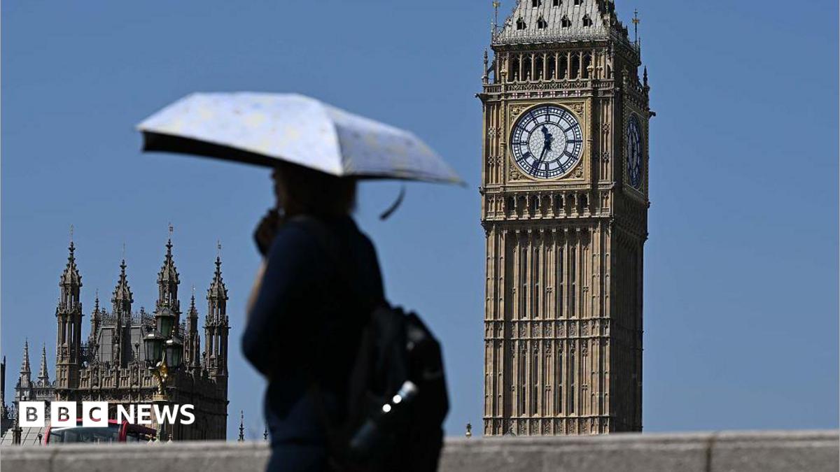 Person walks in front of Big Ben in the heat, carrying an umbrella for shade
