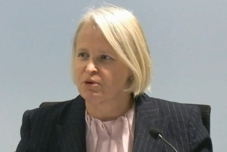 A blonde woman with bob cut wearing a pink dress shirt and a blazer.