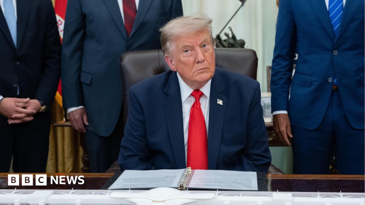 US President Donald Trump sitting in the White House wearing a blue suit jacket, white shirt and red tie.