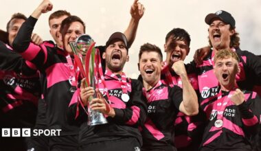 Somerset players wearing pink and black shirts lift the T20 Blast trophy and celebrate