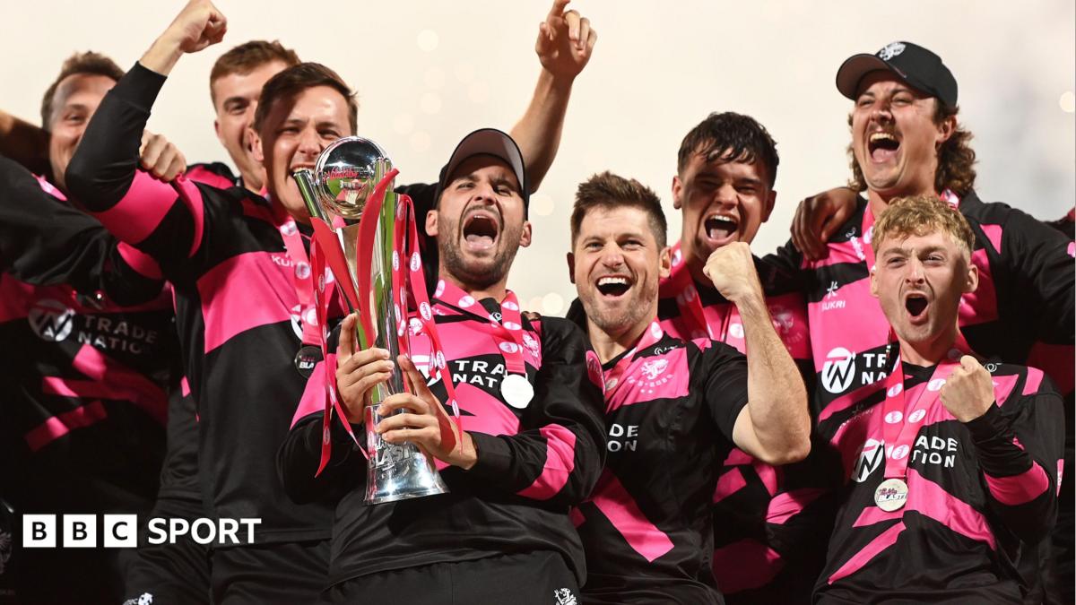Somerset players wearing pink and black shirts lift the T20 Blast trophy and celebrate