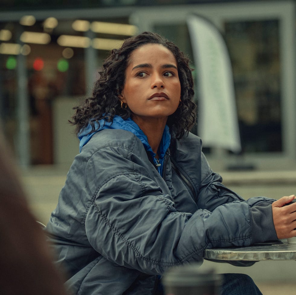 person wearing a jacket, holding a cup at an outdoor table. person wearing a jacket, holding a cup at an outdoor table.