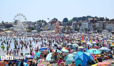 A general view of Weymouth beach during a heatwave in May, with hundreds of people using the beach and a blue sky above.