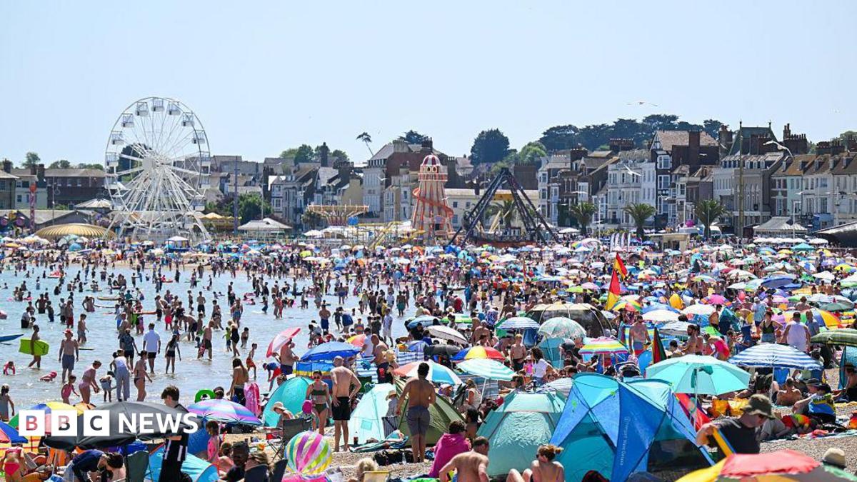 A general view of Weymouth beach during a heatwave in May, with hundreds of people using the beach and a blue sky above.
