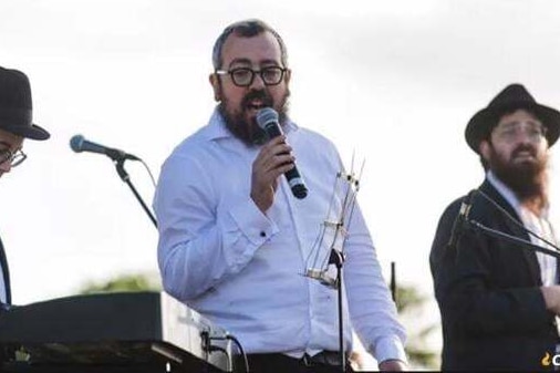 A man holds a microphone while singing into it on an outdoor stage