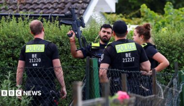 Four police officers are pictured, with one officers holding a gun up