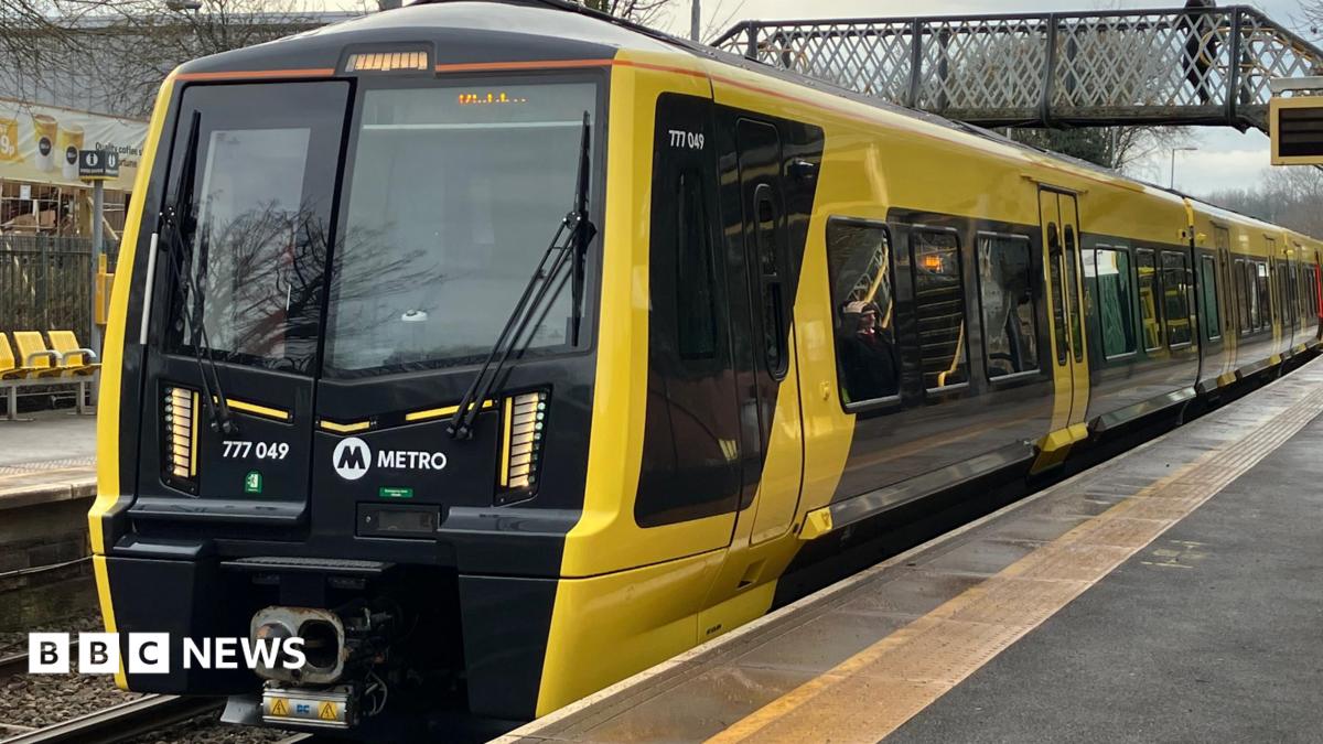 The Merseyrail train is black and yellow, and has stopped at a platform.
