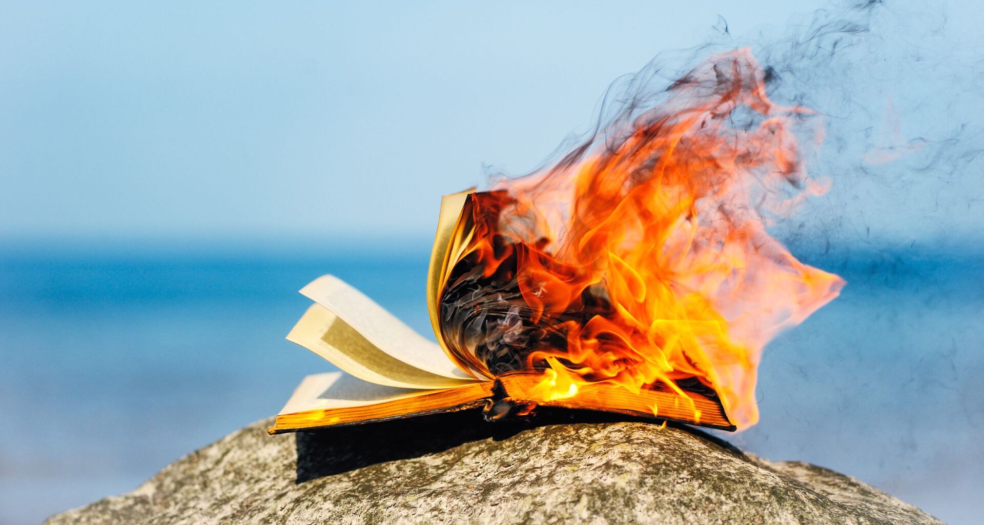 A book burning on a rock by the coast.
