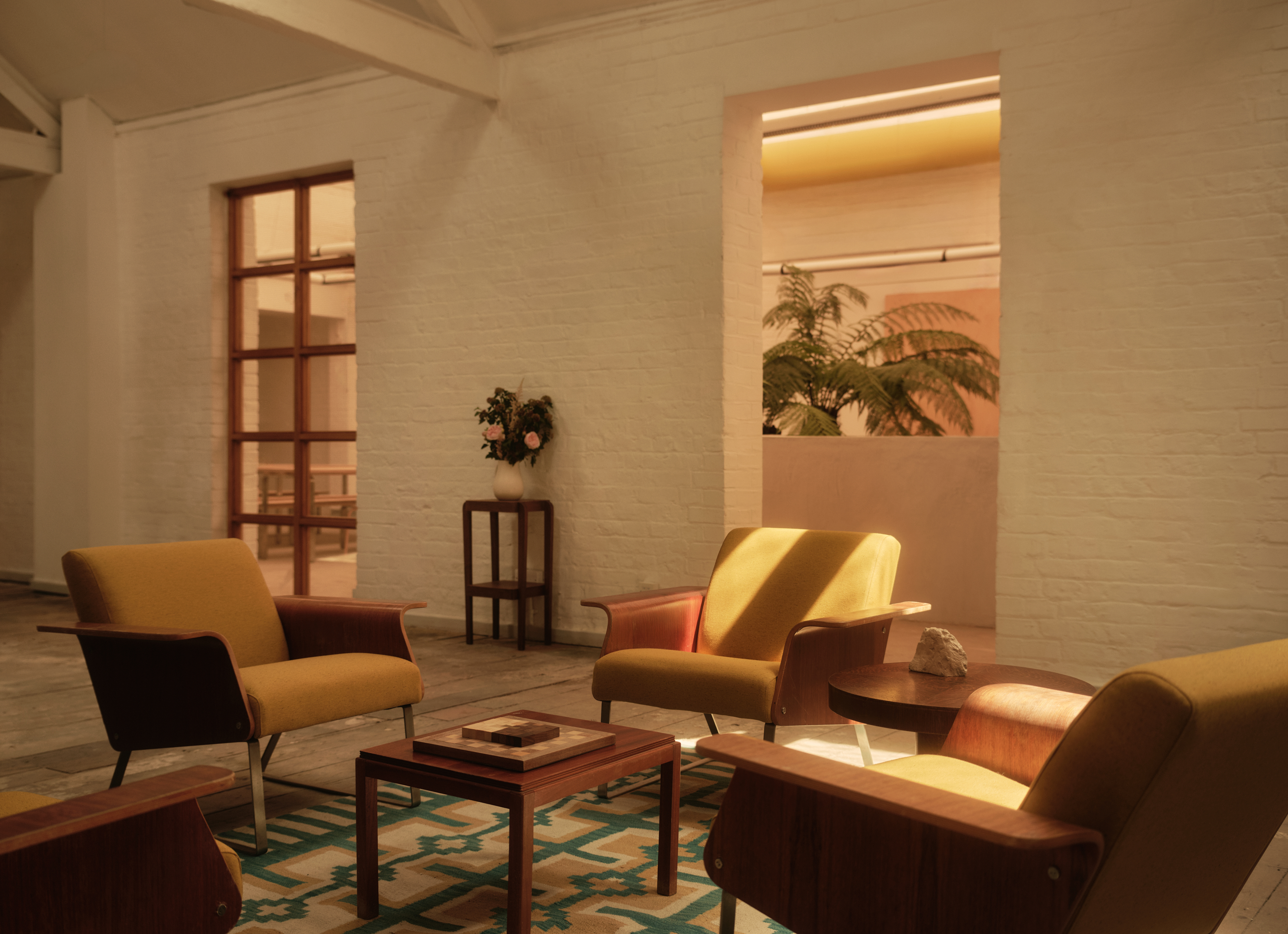 A warmly decorated former warehouse now filled with mid-century modern wooden furniture, colorful pops across floors and walls, statement lighting, glass blocks, and plants.