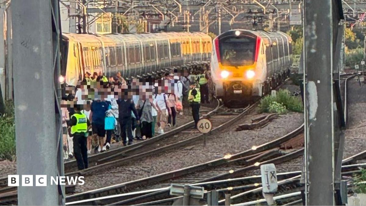 A group of people in single file walk along a train track.