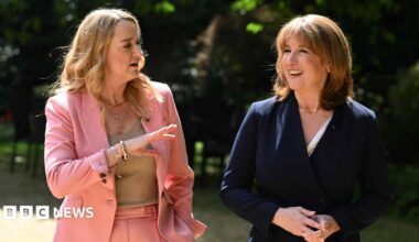 Rachel Reeves on the right, in a blue suit, being interviewed by Laura Kuenssberg on the left, in a pink suit, in a grand room underneath a large chandelier