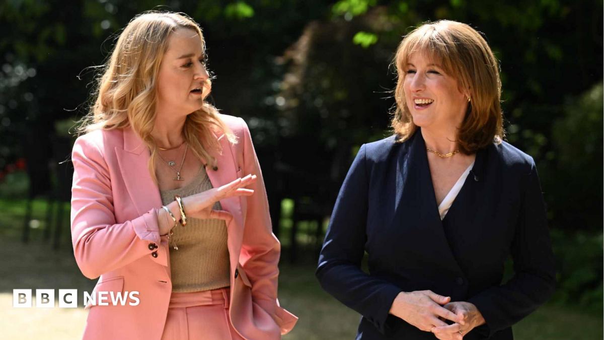 Rachel Reeves on the right, in a blue suit, being interviewed by Laura Kuenssberg on the left, in a pink suit, in a grand room underneath a large chandelier