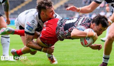 Leigh's David Armstrong, in red shorts and multi-coloured top dives over to score despite a tackle by a Hull FC player, in white shirt.