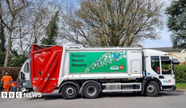 A Biffa recycling lorry is parked on a residential street beside wheelie bins. The vehicle displays a large "Reduce Reuse Recycle" sign and branding from Tandridge District Council and Biffa, with collection staff visible nearby.