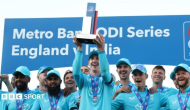 Harry Brook lifts a trophy, stood in front of his England team-mates who are all wearing medals