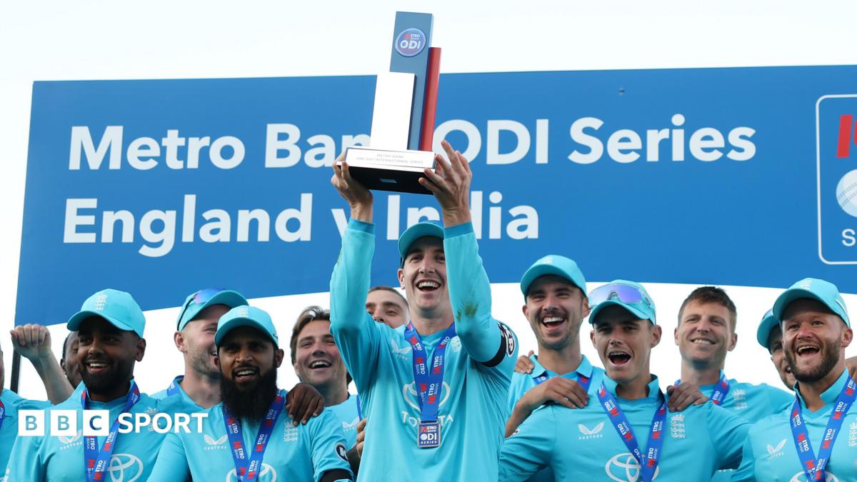 Harry Brook lifts a trophy, stood in front of his England team-mates who are all wearing medals