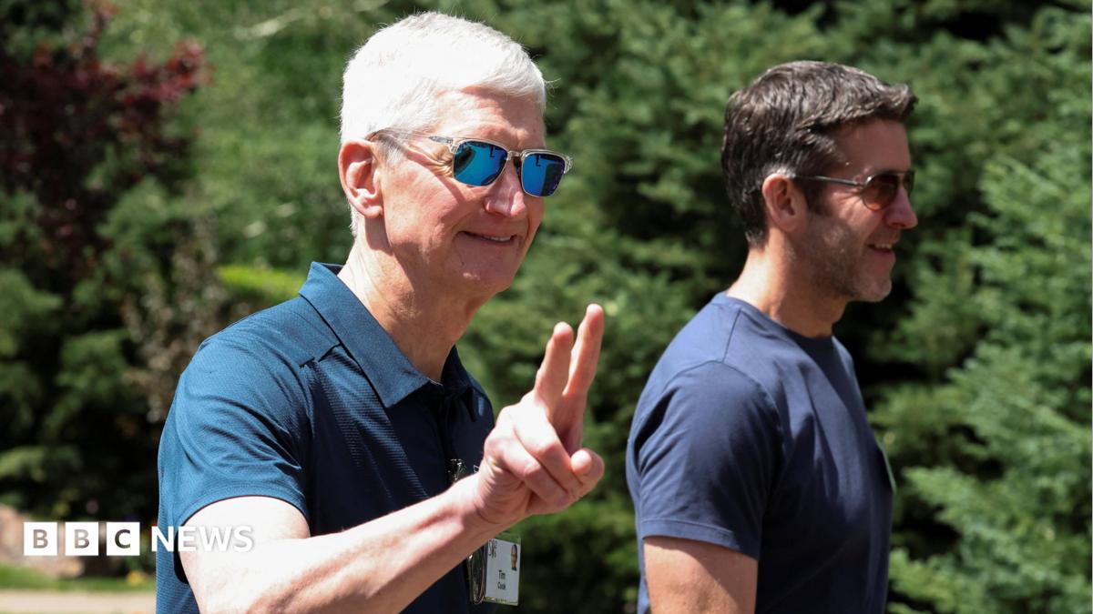 Apple CEO Tim Cook walking outside, throwing up 'peace' fingers, wearing a blue polo shirt and reflective sunglasses. John Ternus, who will replace Cook as CEO later this year, walks beside him, wearing a blue t-shirt and sunglasses.
