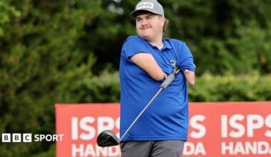 Adam Dalton wearing a blue shirt tucks a golf club under his armpit