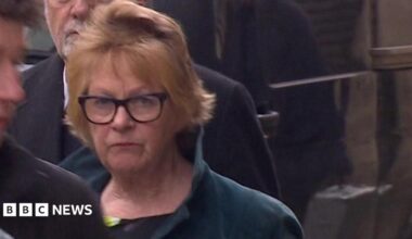 Fiona Hodge is pictured walking into court. She has short, light-coloured hair and is wearing dark-framed glasses. She is wearing a dark green jacket with the collar up. The expression on her face is serious.