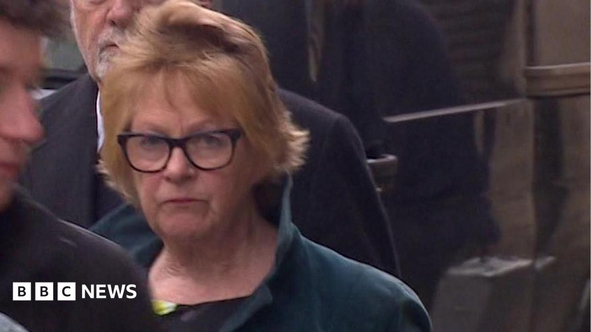 Fiona Hodge is pictured walking into court. She has short, light-coloured hair and is wearing dark-framed glasses. She is wearing a dark green jacket with the collar up. The expression on her face is serious.