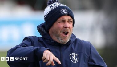 Matt Walker shouting and pointing instructions, wearing a blue and white Kent CC beanie hat and blue padded training jacket