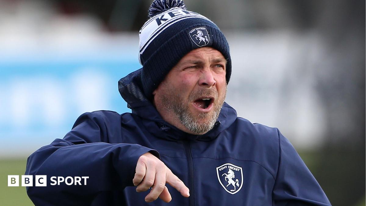 Matt Walker shouting and pointing instructions, wearing a blue and white Kent CC beanie hat and blue padded training jacket