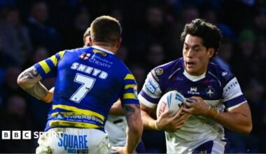 Wakefield's Isaiah Vagana, wearing a white and blue shirt, runs at Warrington's Marc Sneyd