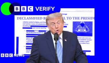 President Trump speaking in front of a microphone with a graphic showing a declassified document behind him.