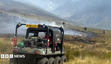 A firefighter damping down hot spots following a moorland wildfire on Tintwistle Moor, above Woodhead Road in Glossop, Derbyshire.