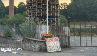 An image of the top of the bonfire, consisting of wood pallets, with a structure resembling a mosque on top. Two placards are below. One reads "secure our borders" while another reads "end the threat of radical Islam".