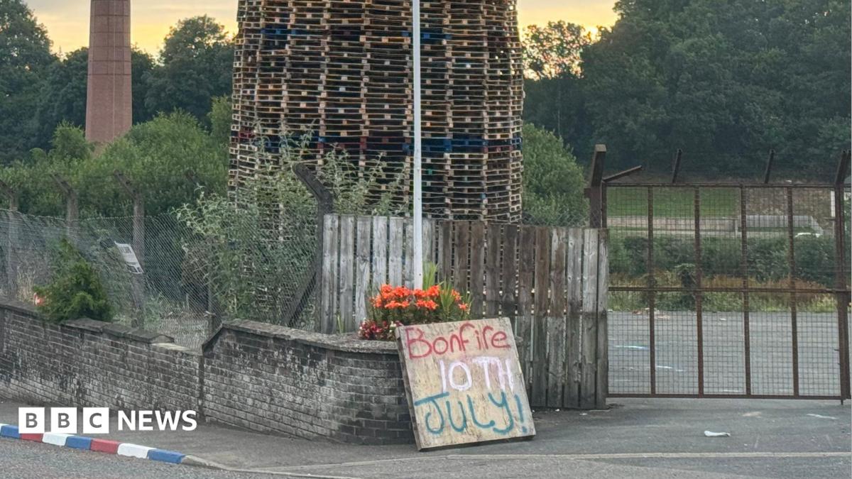 An image of the top of the bonfire, consisting of wood pallets, with a structure resembling a mosque on top. Two placards are below. One reads "secure our borders" while another reads "end the threat of radical Islam".