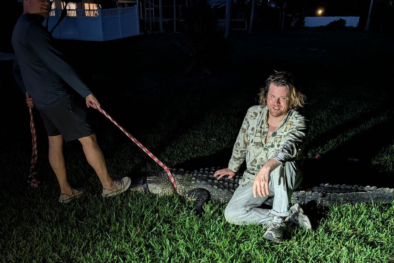 A white man with long brown hair sitting atop an alligator, which has duct tape over its snout and eyes.