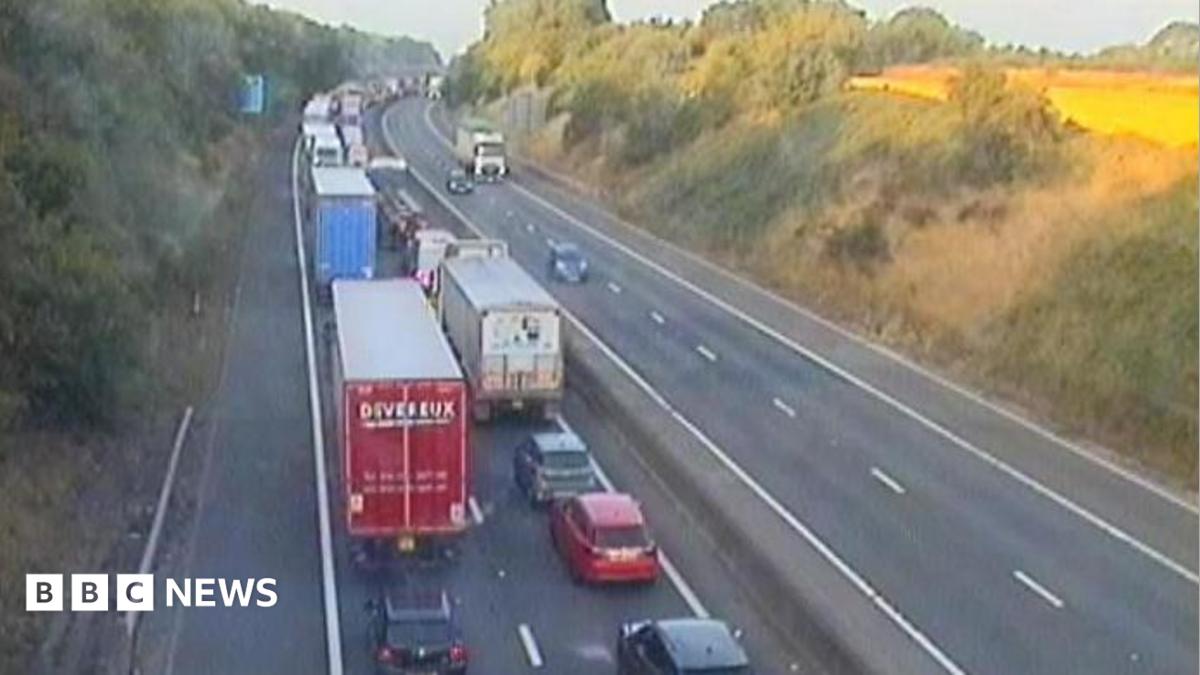 A motorway camera image showing a long queue of vehicles on the carriageway to the left, with three vehicles travelling on the right side of the carriageway